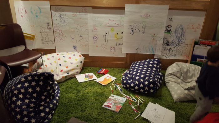 the children's drawing space with colourful pictures on the wall and bean bags scattered over the floor